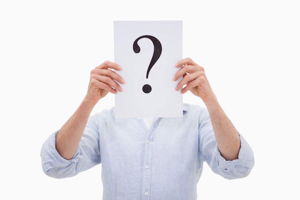 Portrait of a man hiding his face behind a question mark against a white background