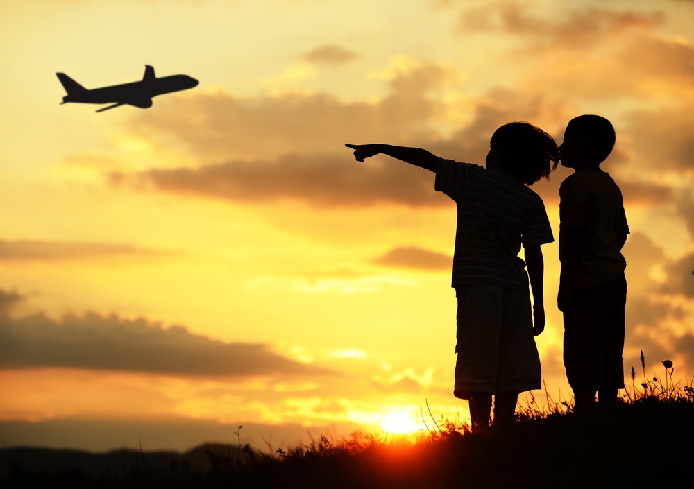 Two kids silhouette on meadow looking at airplane in air